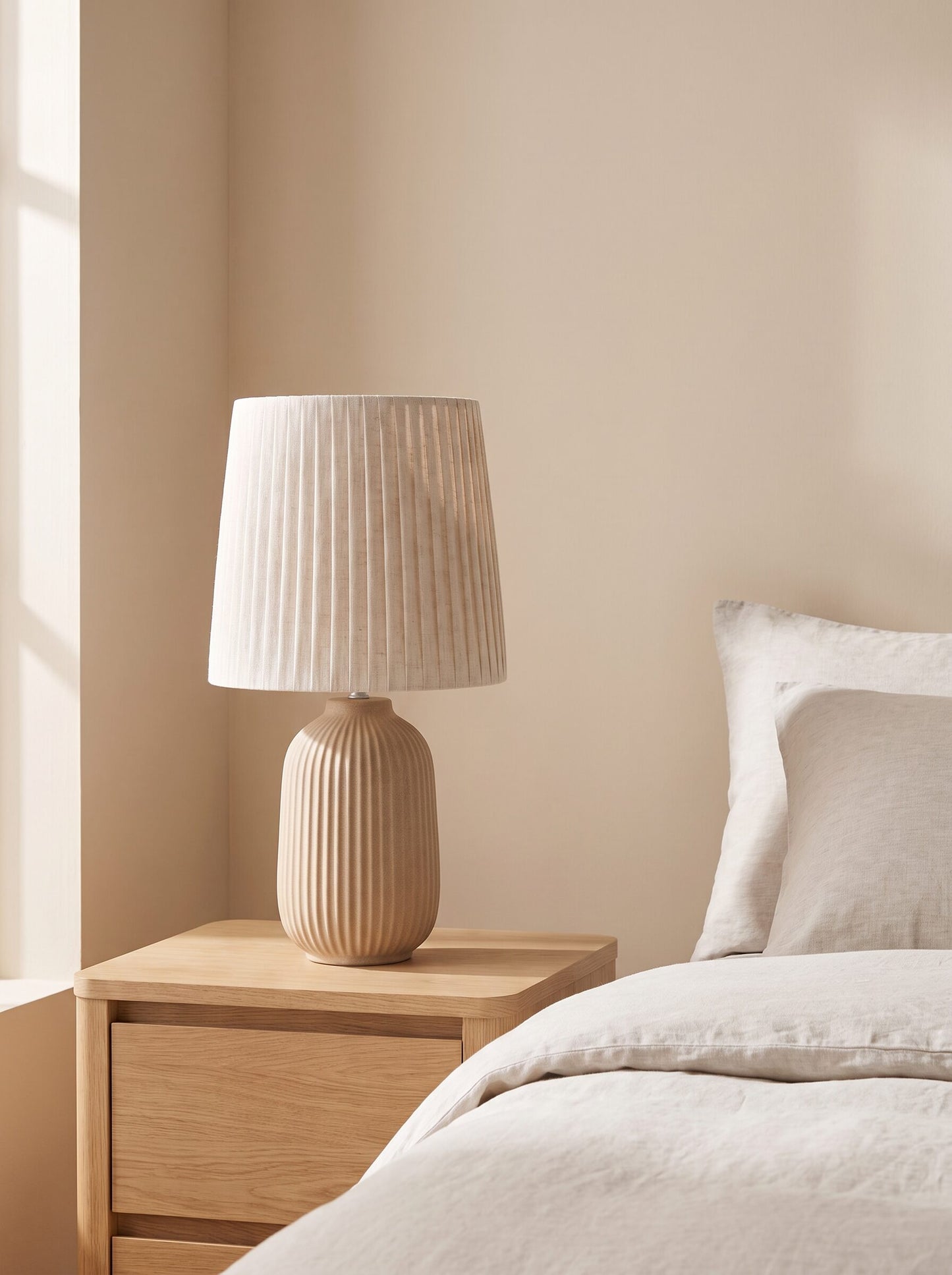 Lámpara de cerámica beige sobre mesita de noche de roble junto a la cama